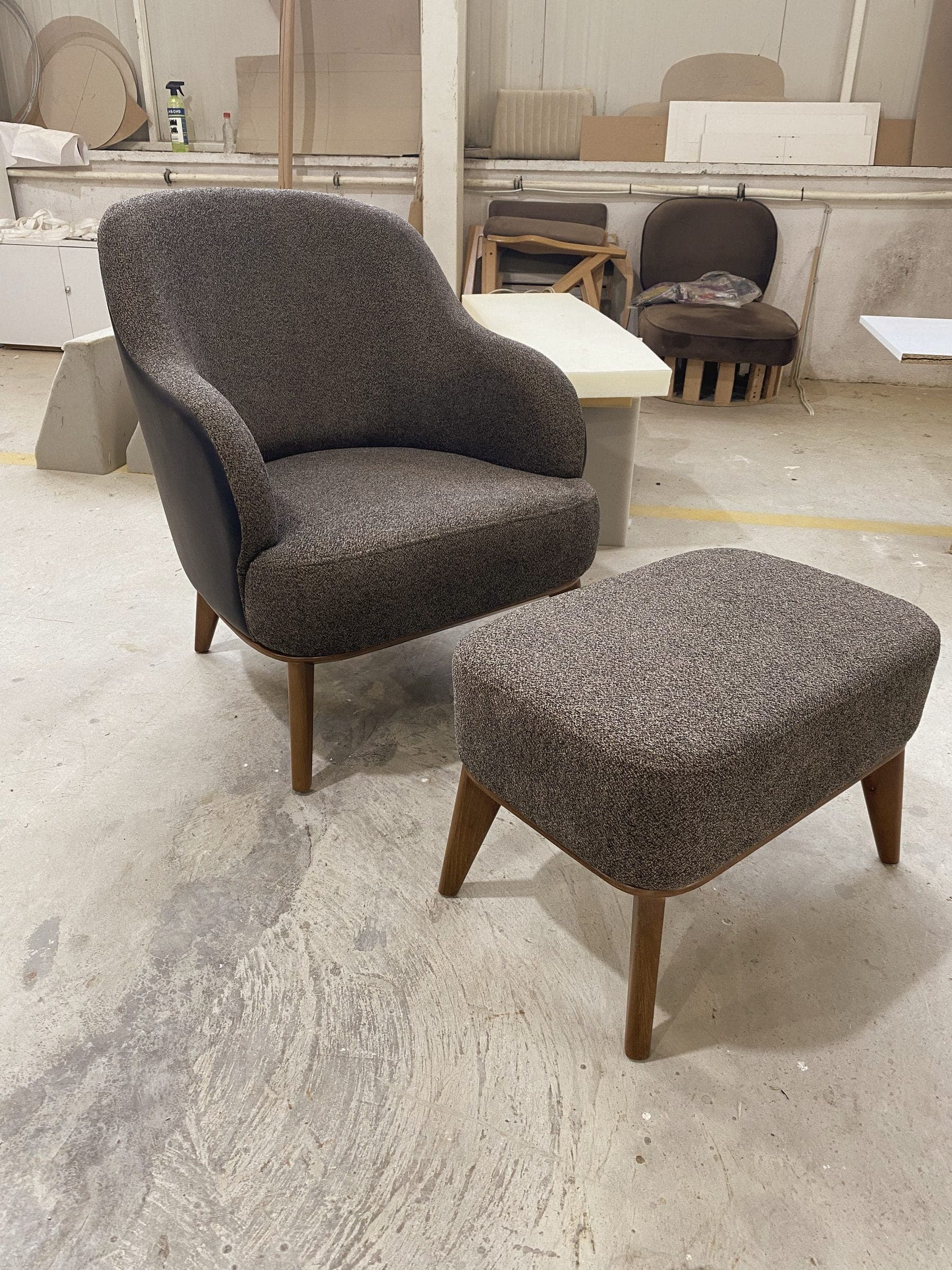 Ein grau gepolsterter Sessel mit passendem Hocker auf Nussbaumfüßen, auf der Produktionsfläche.