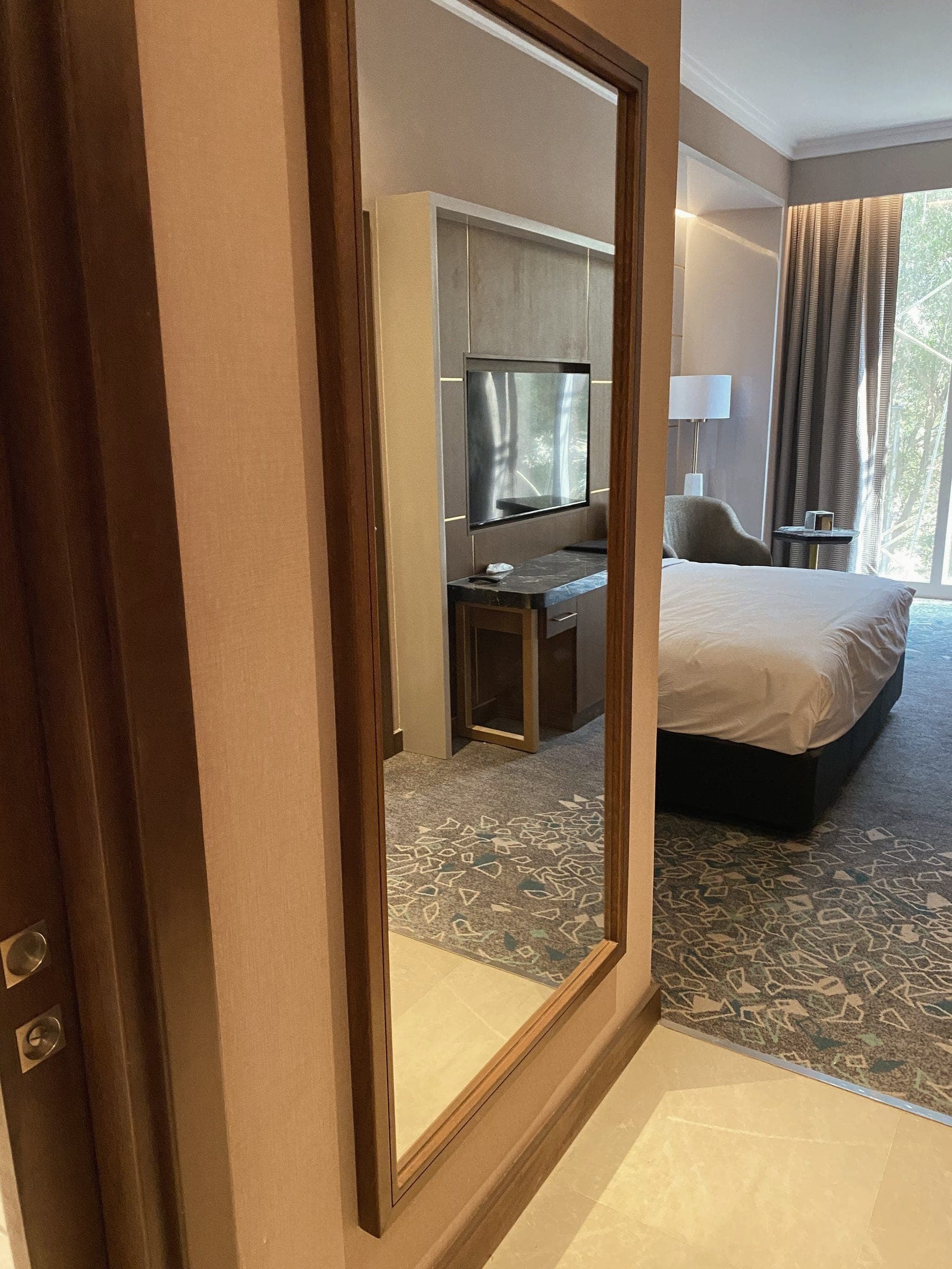 Gerahmter Spiegel mit der Spiegelung von Bett und Fensterwand eines fertigen Gästezimmers.