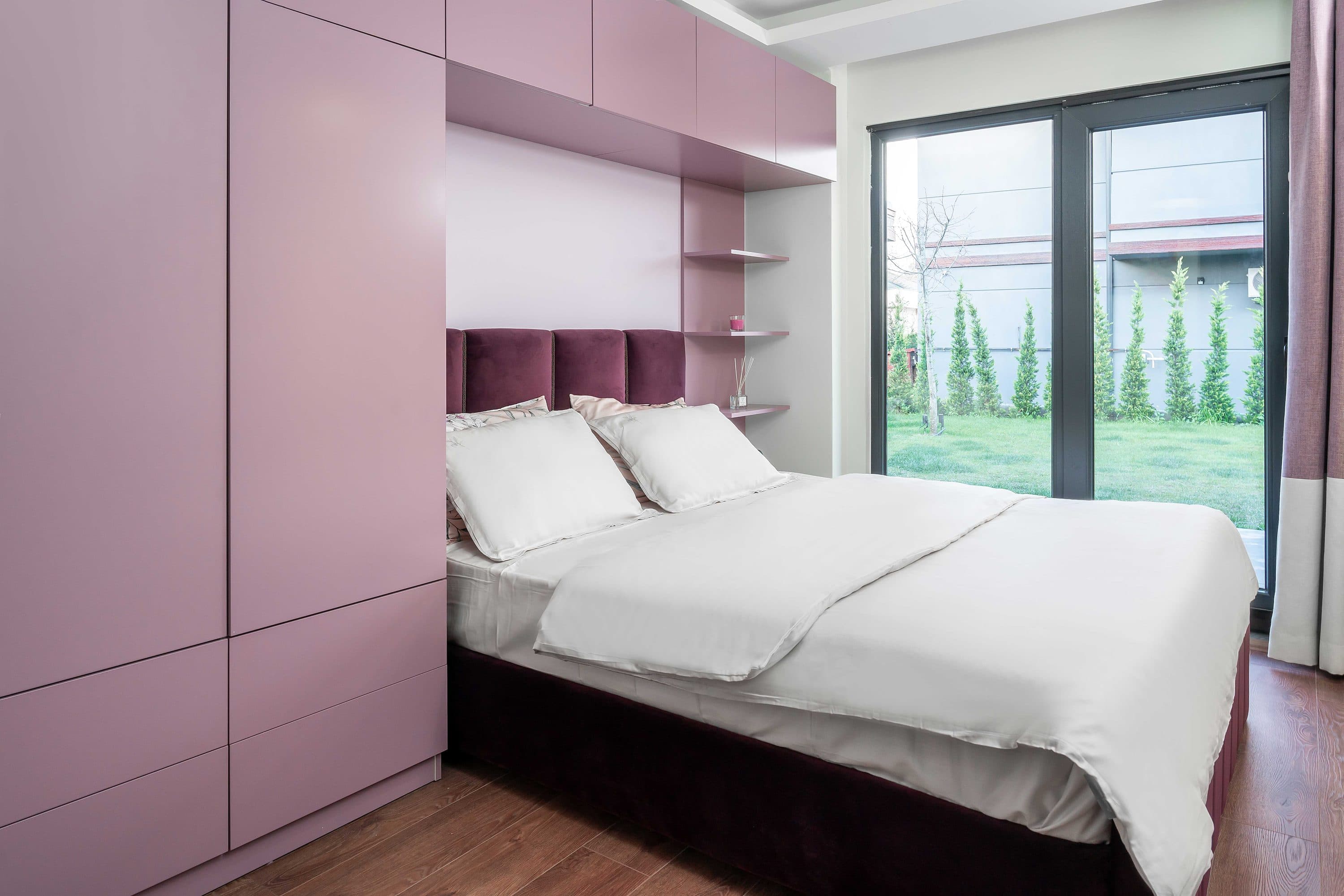 Schlafzimmer mit raumhoher, malvenfarbener Schrankwand bis zu den Glastüren.
