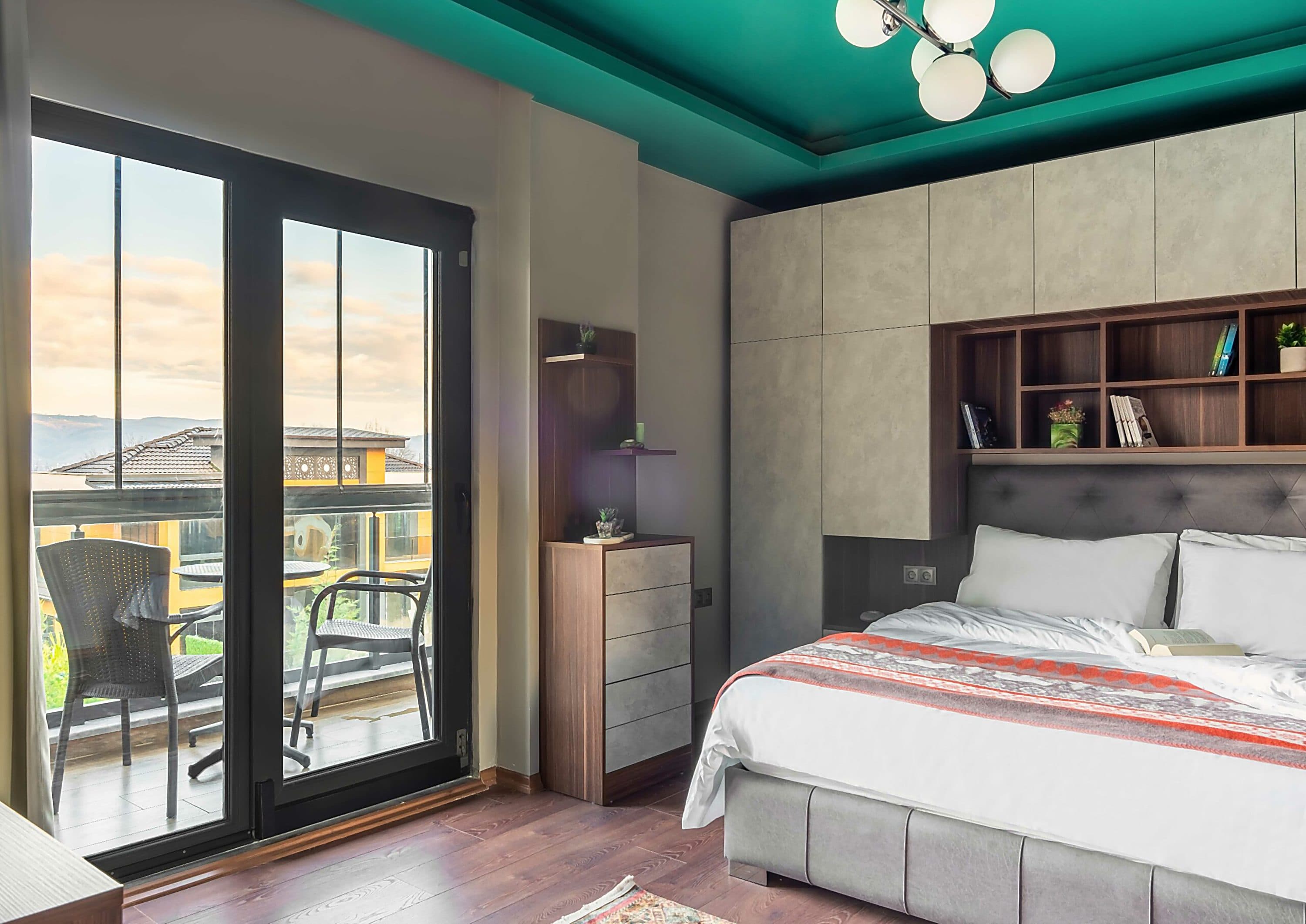 Schlafzimmer mit Glasschiebetüren zum Balkon, grauem Kopfteil und einer niedrigen Kommode.