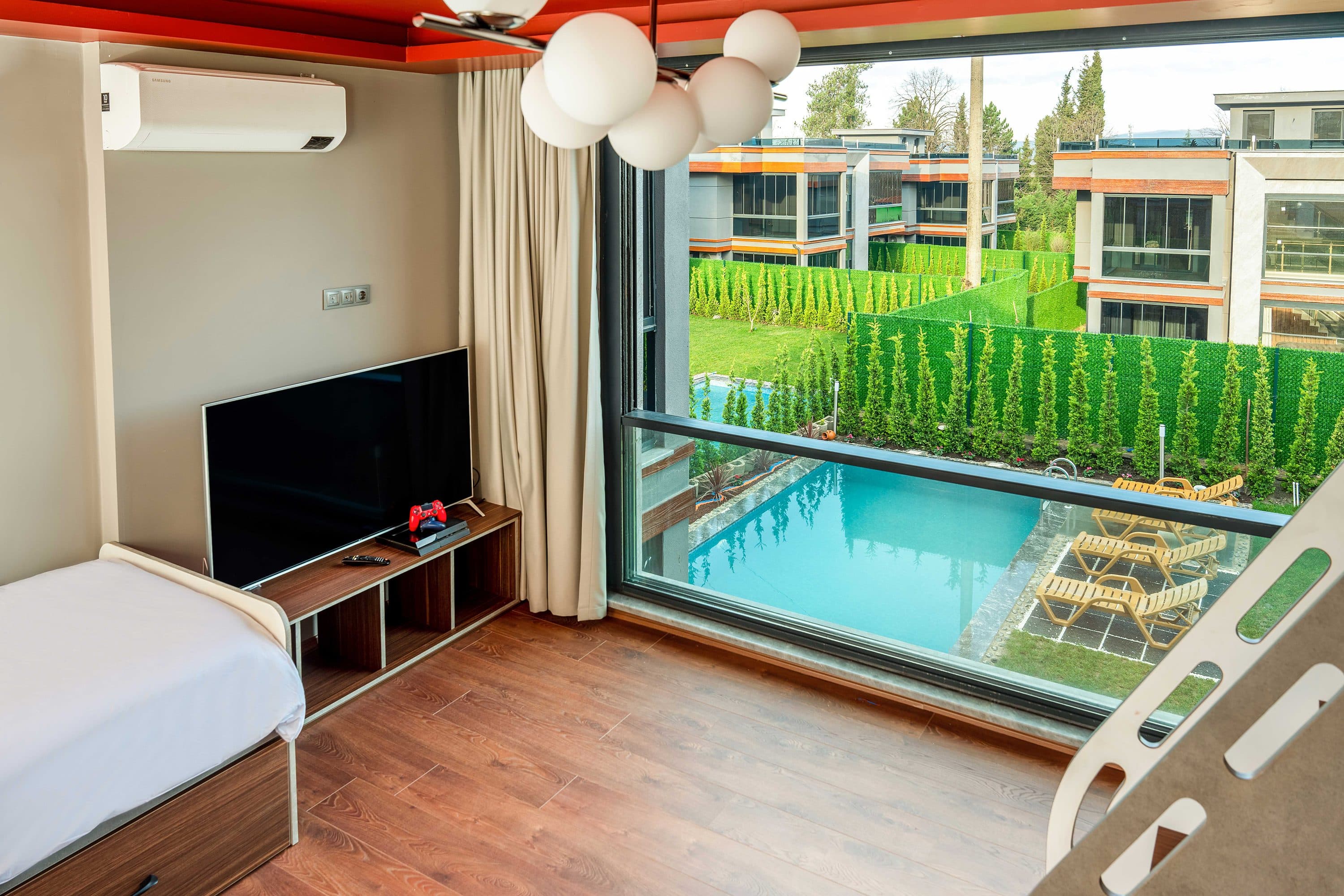 Schlafzimmer mit niedriger TV-Konsole gegenüber einer Glaswand zum Pool.