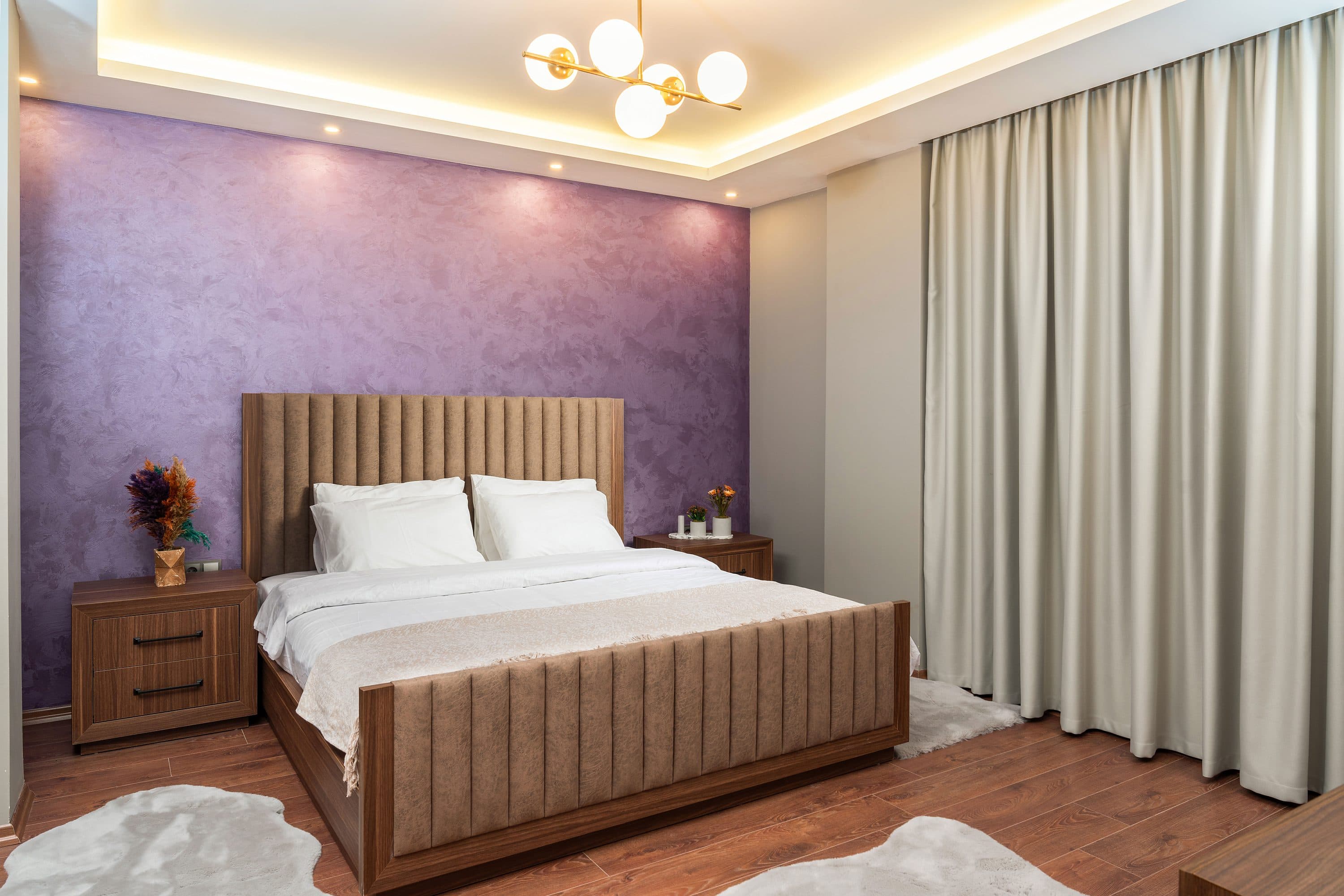 Schlafzimmer mit einem Lamellenkopfteil aus Holz vor einer strukturierten violetten Wand.