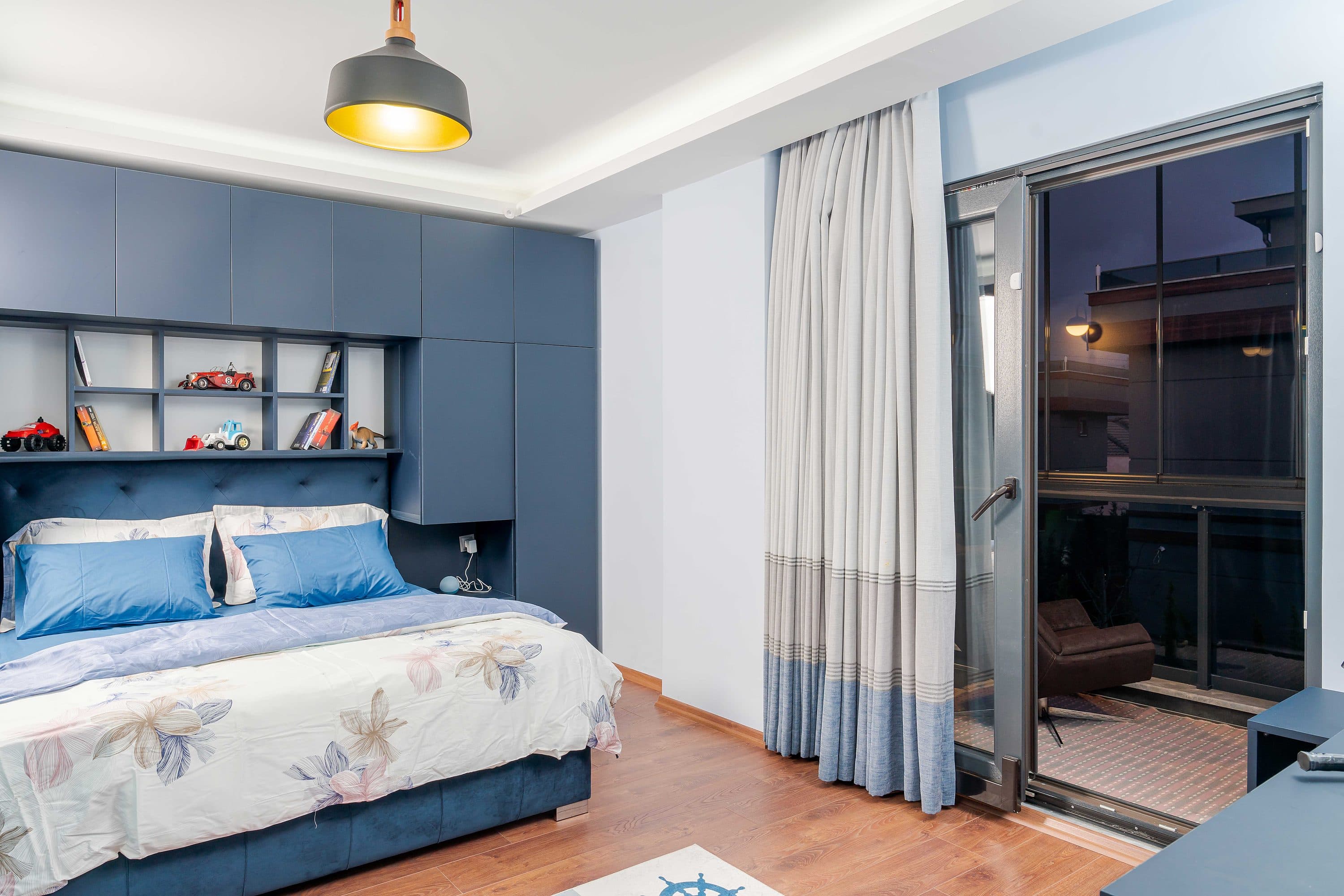 Schlafzimmer mit blaugrauer Regal- und Kopfteilwand, als eine Einheit gebaut.