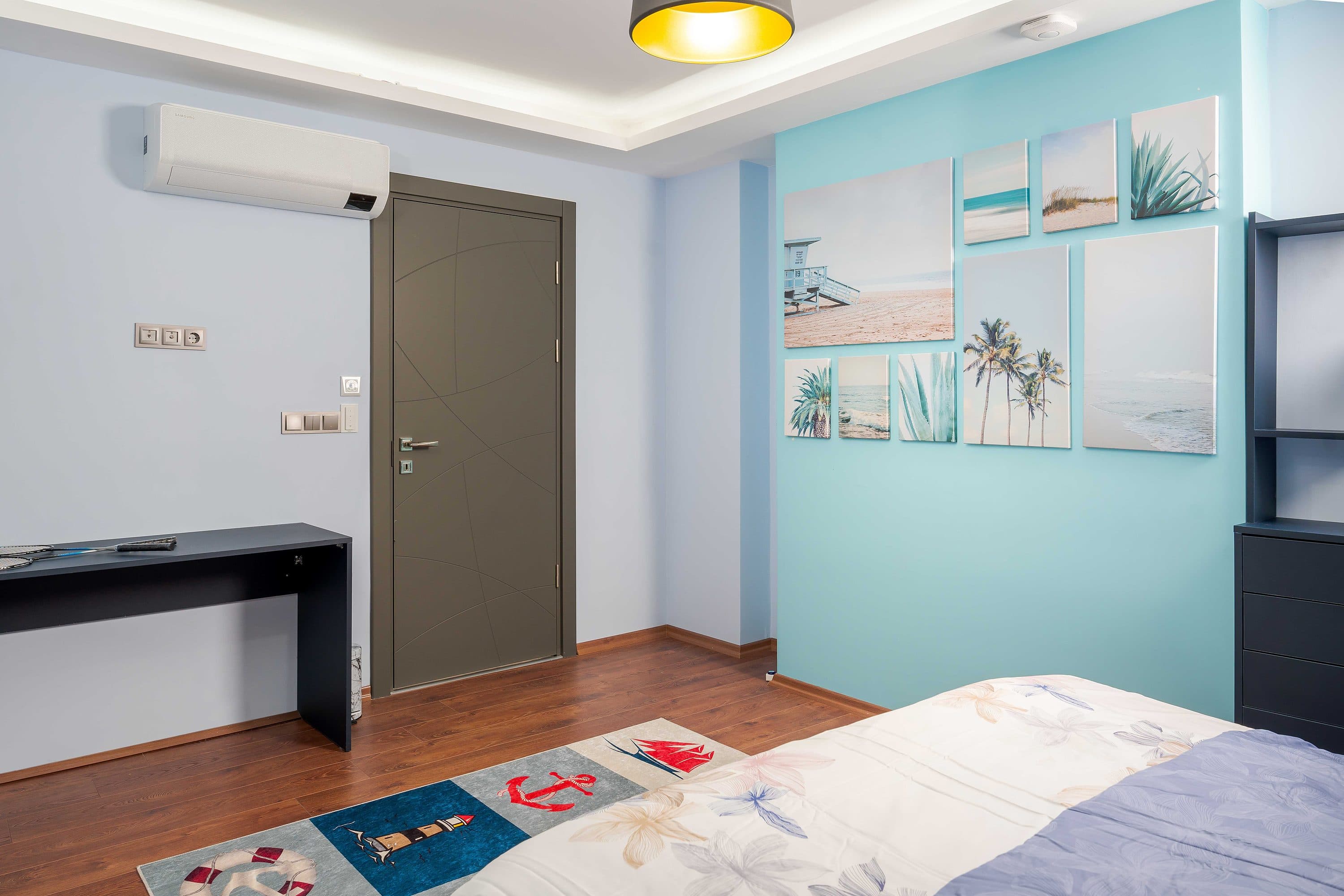 Hellblaues Schlafzimmer mit wandhängendem Schreibtisch, gerahmten Drucken und einer lackierten Holztür.
