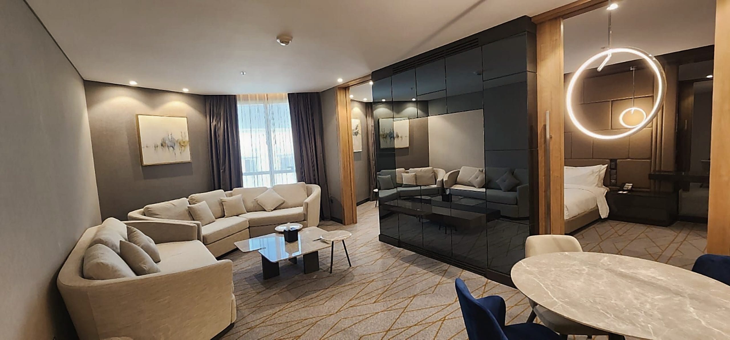 Wohnbereich der Suite im Holiday Inn Al Khobar: Polsterecke, runder Tisch und eine Rauchglastrennwand zum Schlafzimmer.